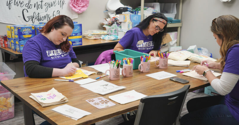 3 Women Decorating Period Packs in a Purple Shirt 